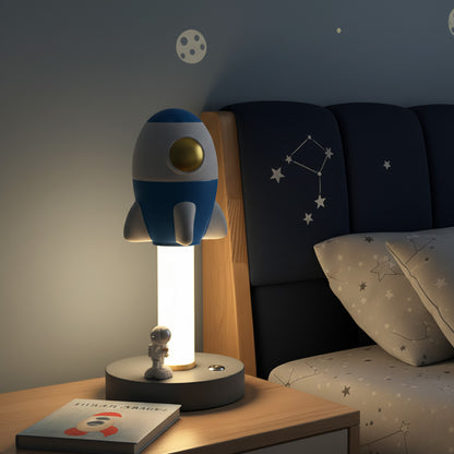 Rocket-shaped lamp on a nightstand with a starry-themed bed in the background