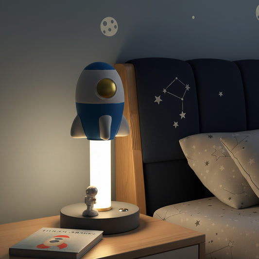 Rocket-shaped lamp on a nightstand with a starry-themed bed in the background