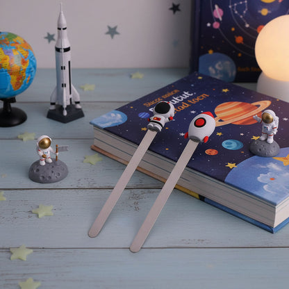 Two space-themed bookmarks on a book with astronaut and rocket decorations.