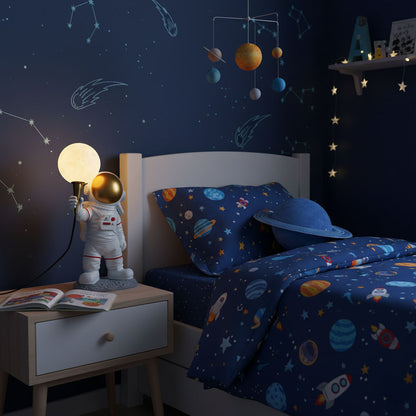 Children's bedroom with space-themed bedding and decor, including an astronaut lamp.