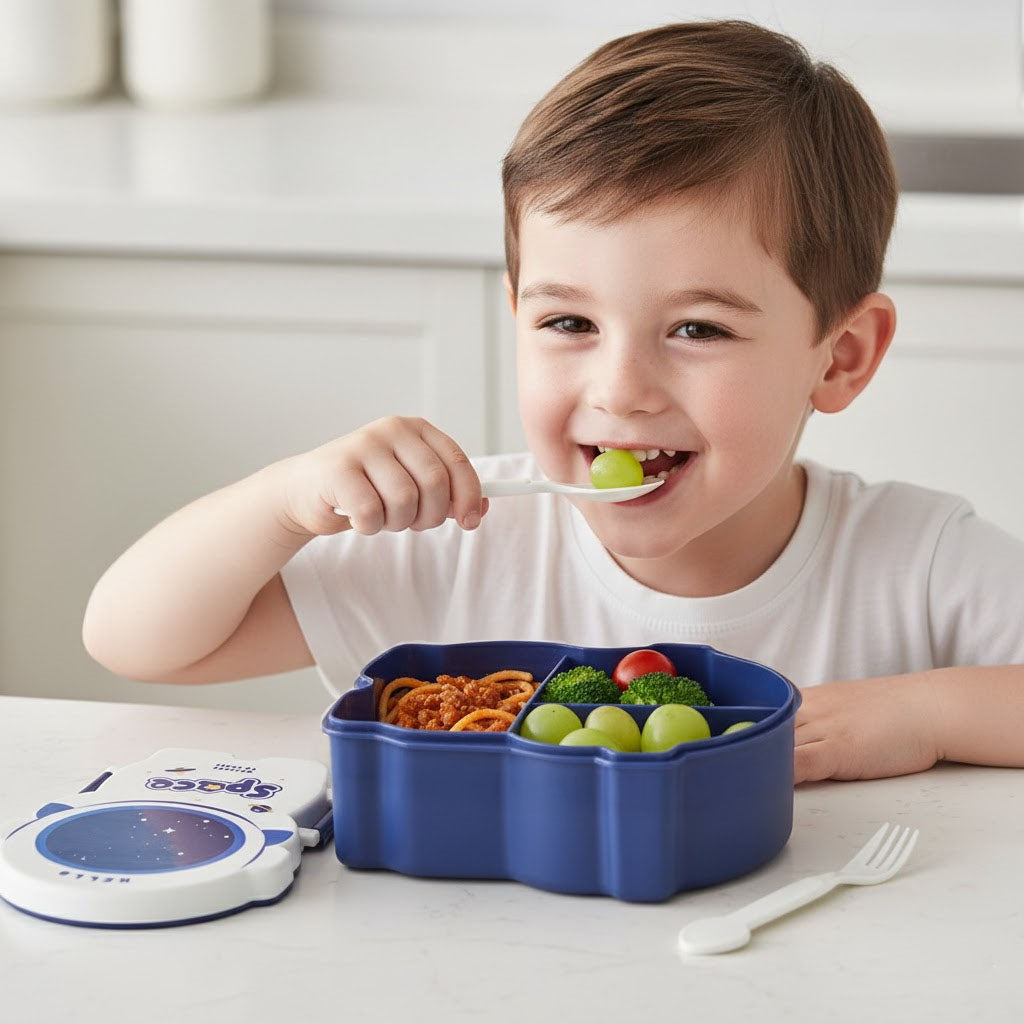 Child eating from a blue compartmentalised lunch box with food, sitting at a table.
